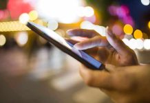 A person's hand using a smartphone in a city at night with blurred lights in the background