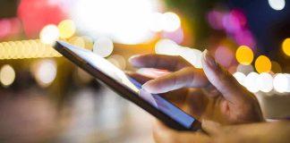 A person's hand using a smartphone in a city at night with blurred lights in the background