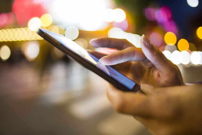 shutterstock_160559990.jpg A person's hand using a smartphone in a city at night with blurred lights in the background
