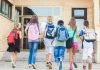 Group of children walking towards a school entrance with backpacks