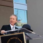 A man in formal attire speaking at a podium during a Hollywood Walk of Fame ceremony
