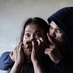 Man holding woman's mouth, gesturing silence.