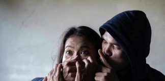 Man holding woman's mouth, gesturing silence.
