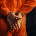 Person in orange jumpsuit with handcuffs behind back
