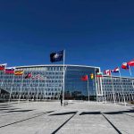 Flags outside NATO headquarters building under clear blue sky