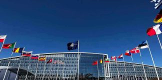 Flags outside NATO headquarters building under clear blue sky