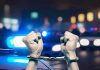Handcuffed hands raised, police cars with lights on.
