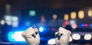Handcuffed hands raised, police cars with lights on.