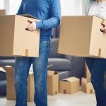 Two people carrying cardboard boxes indoors