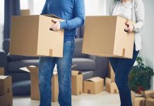 Two people carrying cardboard boxes indoors