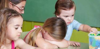 Children at a table with building blocks, one child appears upset
