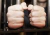 Hands gripping jail cell bars tightly.