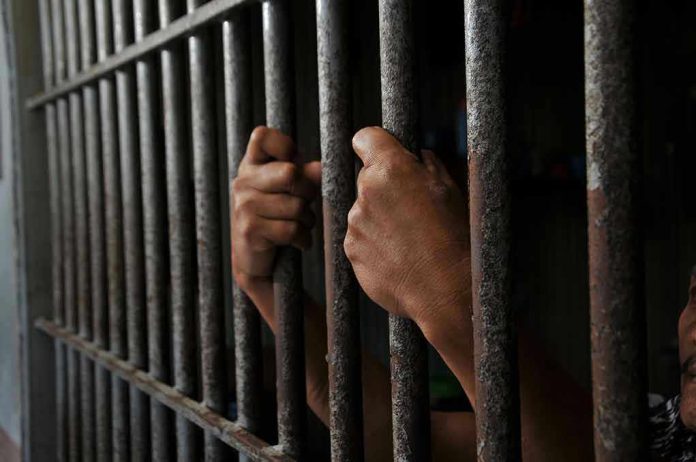 Hands gripping prison cell bars tightly.