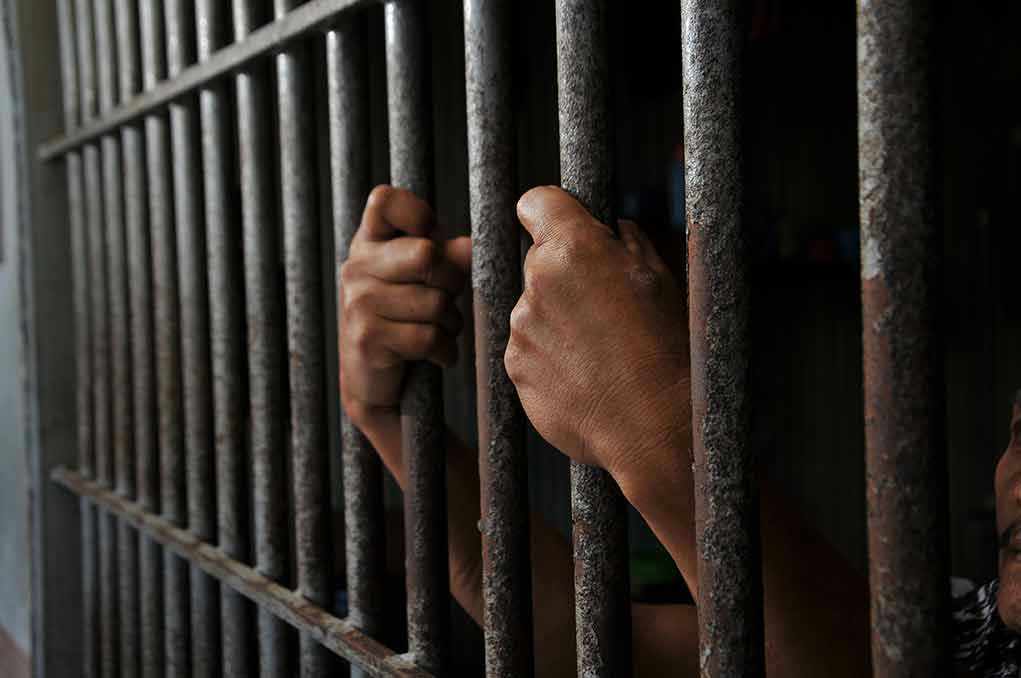 Hands gripping prison cell bars tightly.