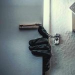 Gloved hand opening door with security chain.