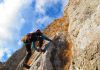 A climber ascending a rocky cliff under a blue sky