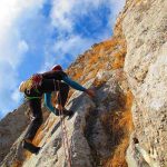 A climber ascending a rocky cliff under a blue sky