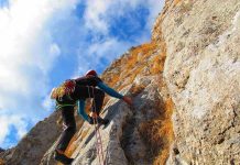 A climber ascending a rocky cliff under a blue sky