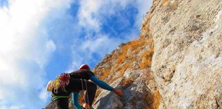 A climber ascending a rocky cliff under a blue sky