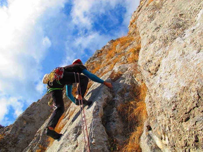 A climber ascending a rocky cliff under a blue sky