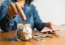 Person placing a coin into a savings jar labeled SAVINGS