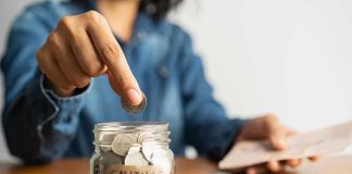 Person placing a coin into a savings jar labeled SAVINGS