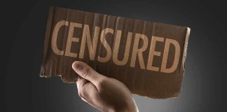 A hand holding a cardboard sign that reads CENSORED