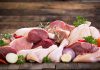Assorted raw meat with vegetables on wooden table.
