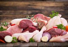 Assorted raw meat with vegetables on wooden table.